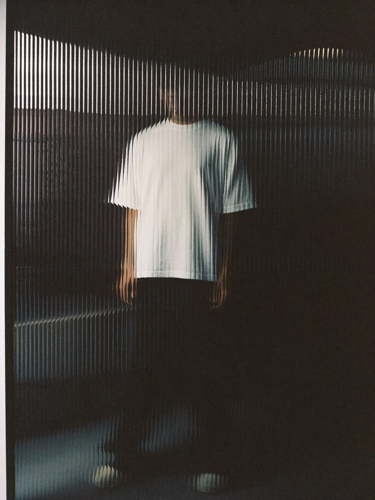 Silhouette in t-shirt bianca dietro un vetro cannettato, foto in pellicola: l'identità di chi lavora con HABA Studio si rispetta, non si espone